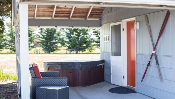 Un espace extérieur abrité avec des sièges, un jacuzzi, une porte et une paire de skis appuyés contre le mur.