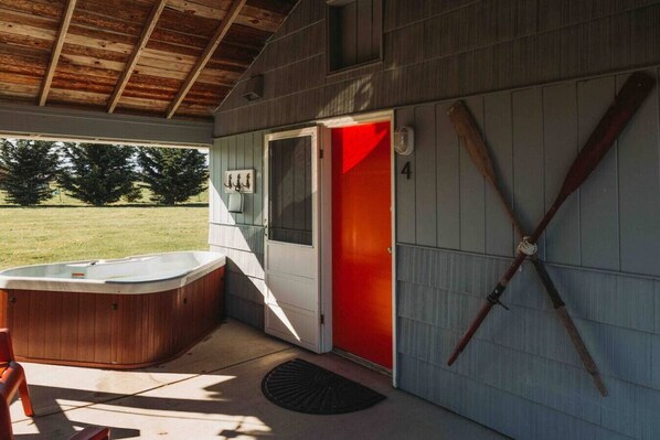 Un espacio al aire libre cubierto con jacuzzi, una puerta roja y una terraza de madera.