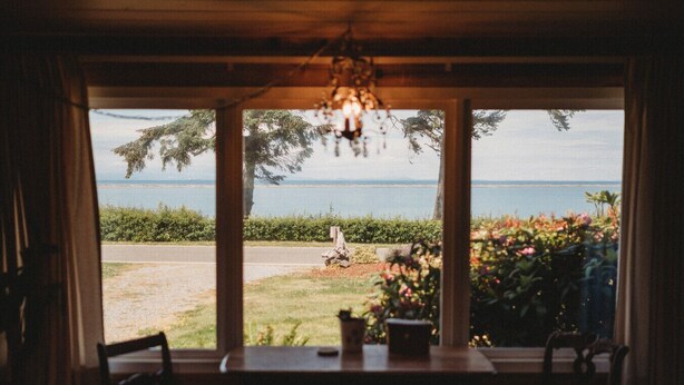 A room with a large window overlooking a garden and a body of water.