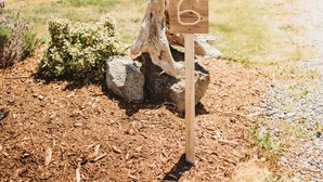A wooden sign with the number 6 in a garden area with mulch, rocks, and a building in the background.