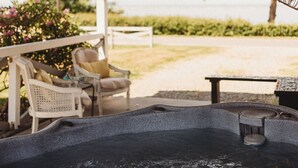 A covered outdoor area with a hot tub, seating, and a view of the outdoors.
