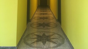 Un pasillo con paredes amarillas y piso estampado, que conduce a una puerta al final.