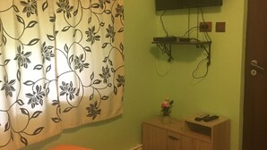 Un dormitorio con cama, televisión montada en la pared, un armario de madera y cortina con estampado floral.