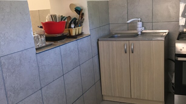 Una cocina con baldosas grises y beige, un fregadero, un armario de madera y un cuenco rojo con utensilios.