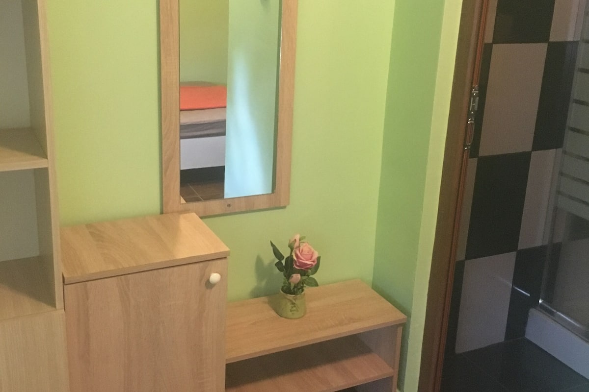 A bathroom with a wooden vanity, a mirror, and a small shelf with a vase of flowers.