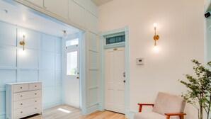 A room with a wooden floor, a white dresser, a beige armchair, and a door with a blue trim. - Suite 3 | Historic Art City Inn (Springville)