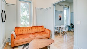 A room with a sofa, a coffee table, and a dining area with chairs and a table. - Suite 3 | Historic Art City Inn (Springville)