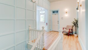 A hallway with a wooden staircase, a door, a chair, and a potted plant. - Suite 4 | Historic Art City Inn (Springville)