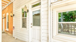 A white building with a brick section, a door labeled "Suite 6", and a window with a view of greenery. - Suite 6 | Historic Art City Inn (Springville)
