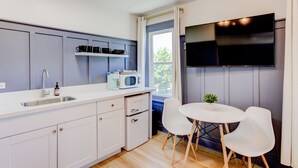 Una cucina moderna con forno a microonde integrato, lavello e piccolo frigorifero. C'è un'area pranzo con tavolo e sedie, e un televisore montato a parete.