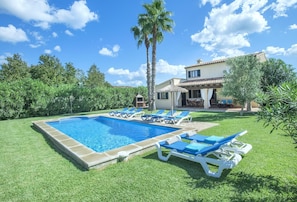 Piscina con sillas de descanso y una casa al fondo.