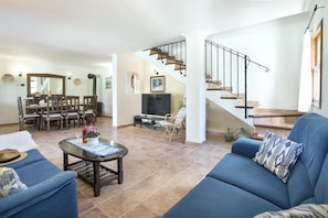 Amplia sala de estar con un sofá azul, un comedor con muebles de madera y una escalera con barandilla de metal.