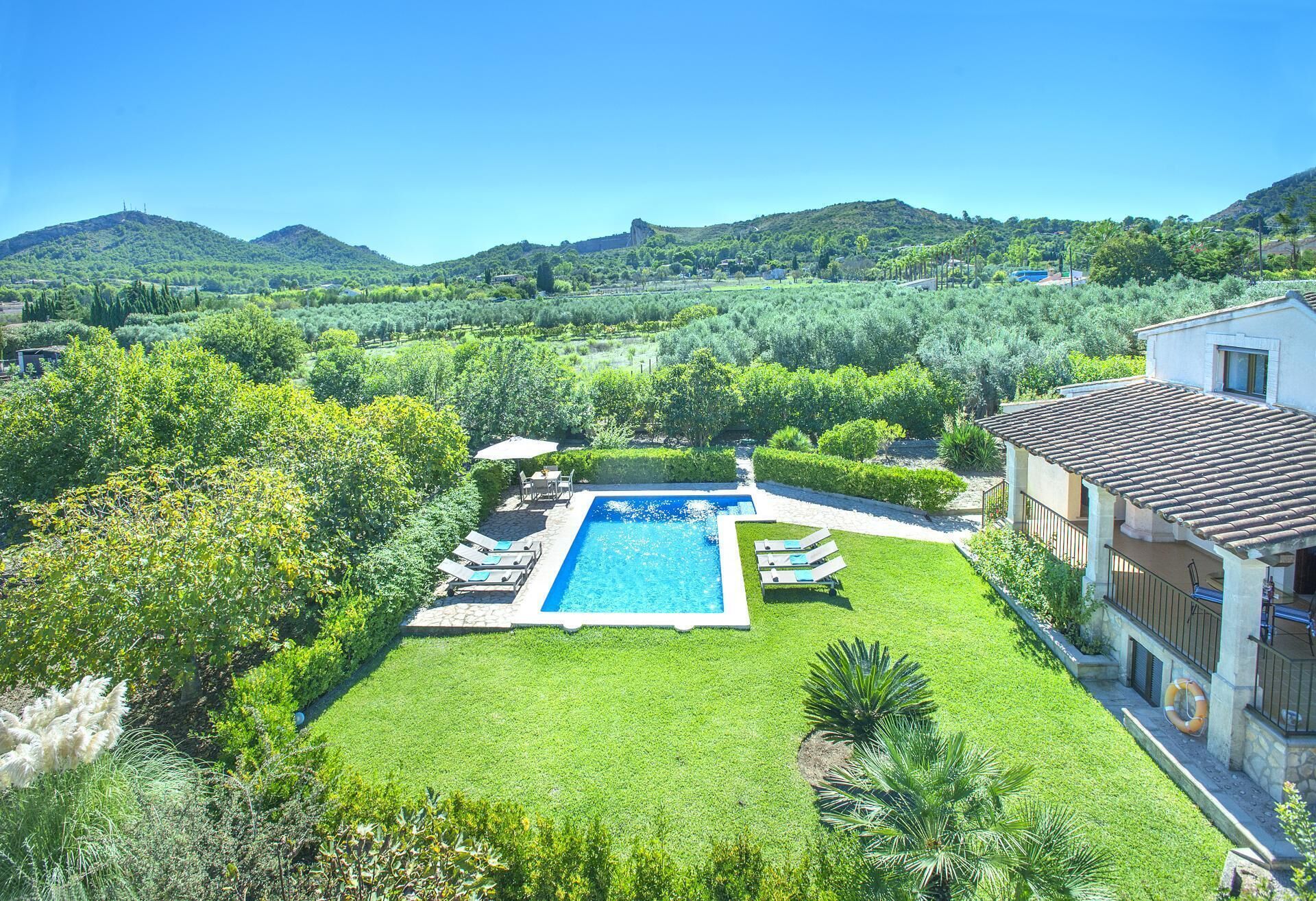 A pool surrounded by a well-maintained lawn, with a house in the background and hills in the distance.