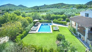 Una piscina rodeada de un césped cuidado, con una casa al fondo y colinas en la distancia.