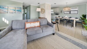 Ein modernes Wohnzimmer mit einem grauen Sofa, einem Essbereich mit einer Chandelier und einer Küche im Hintergrund.