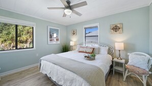 Ein Schlafzimmer mit Bett, Deckenventilator, Fenster mit Blick auf Palmen und einer an der Wand befestigten Kompassdekoration.