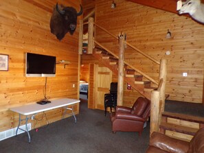 A wooden interior with a mounted buffalo head, a television, a desk, a leather chair, and a staircase. - The Outpost Lodge  (Pierre)