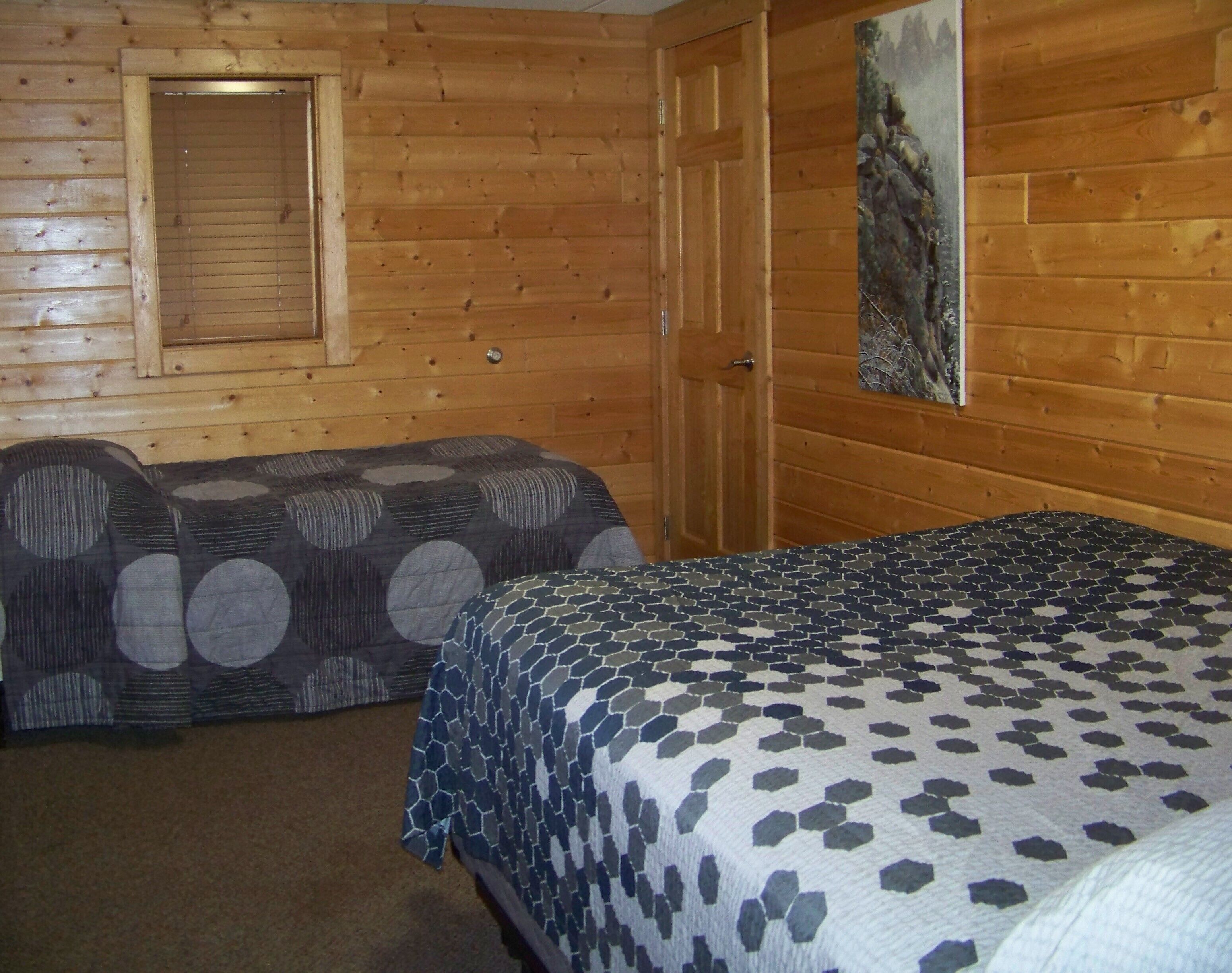 A wooden cabin room with two beds, a window, and a door.