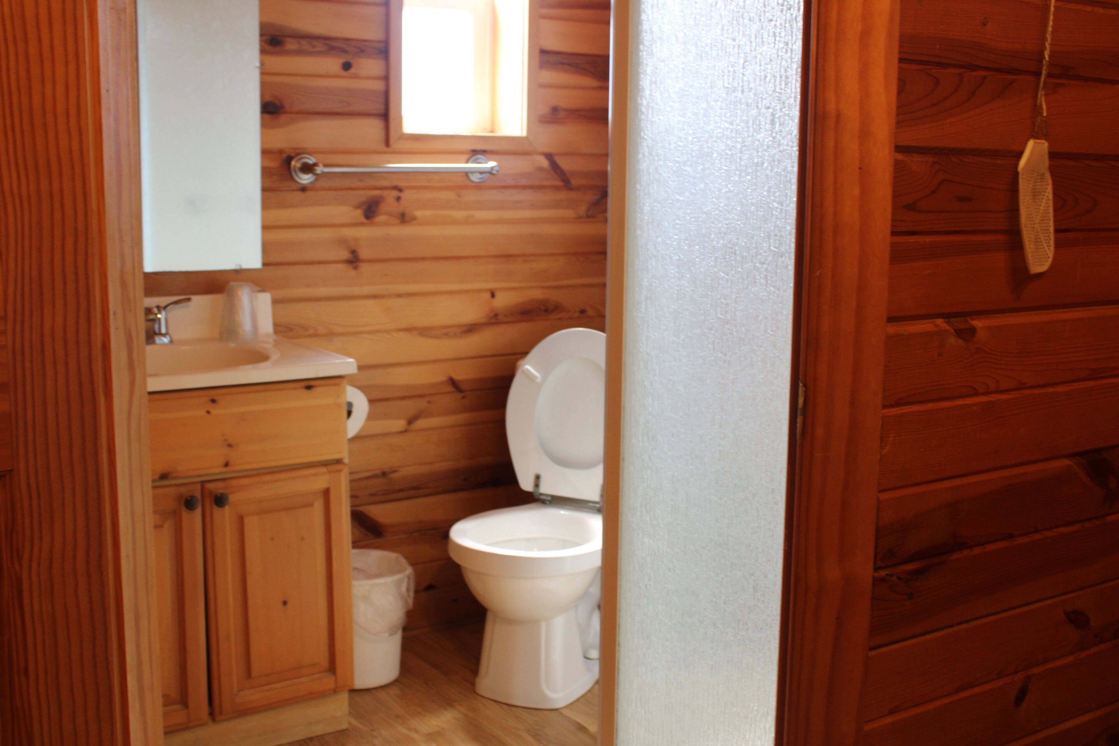 A wooden cabin bathroom with a toilet, sink, and mirror.