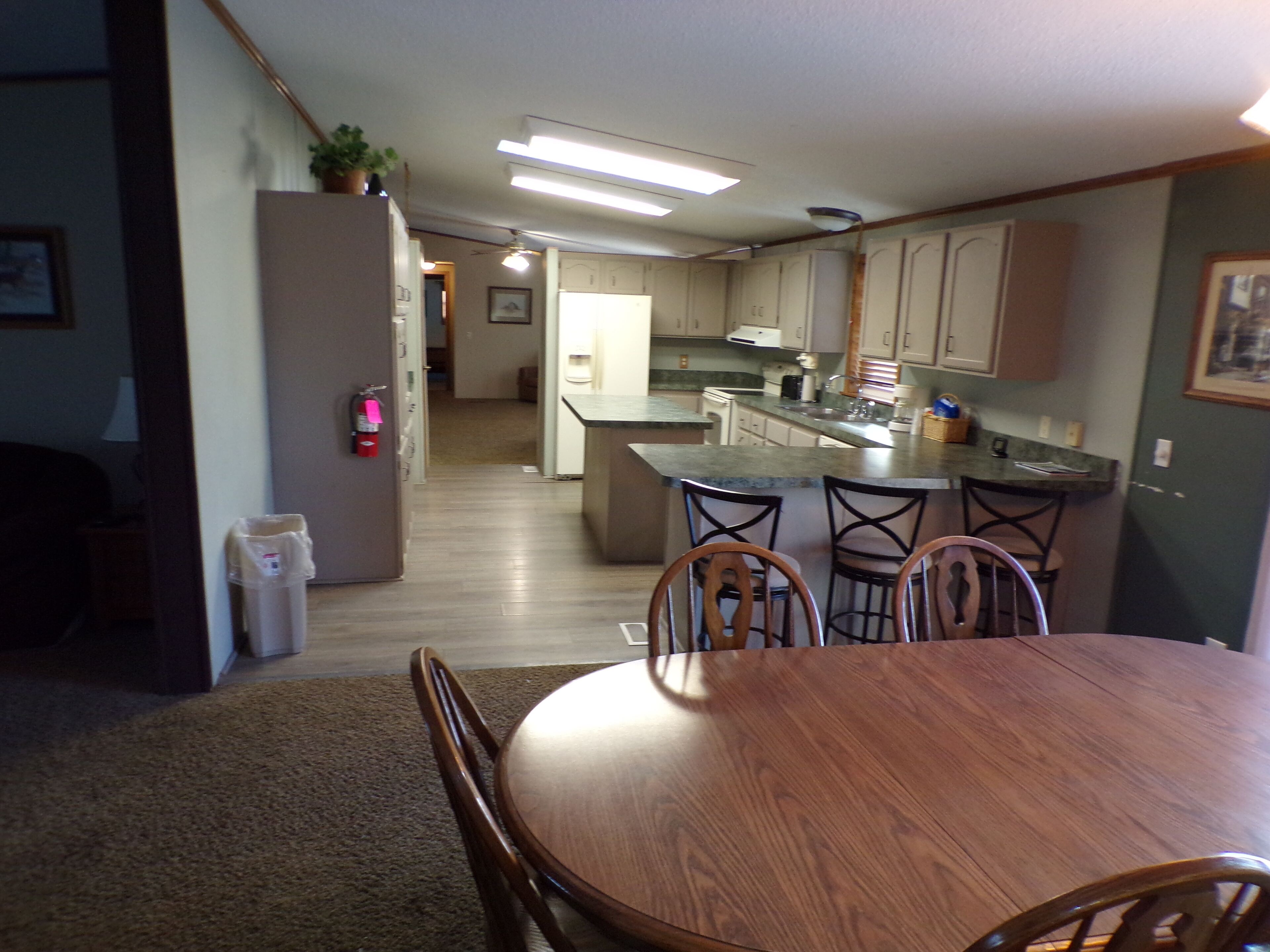 A compact kitchen with a central island, wooden dining table, and chairs. A fire extinguisher is mounted on the wall.