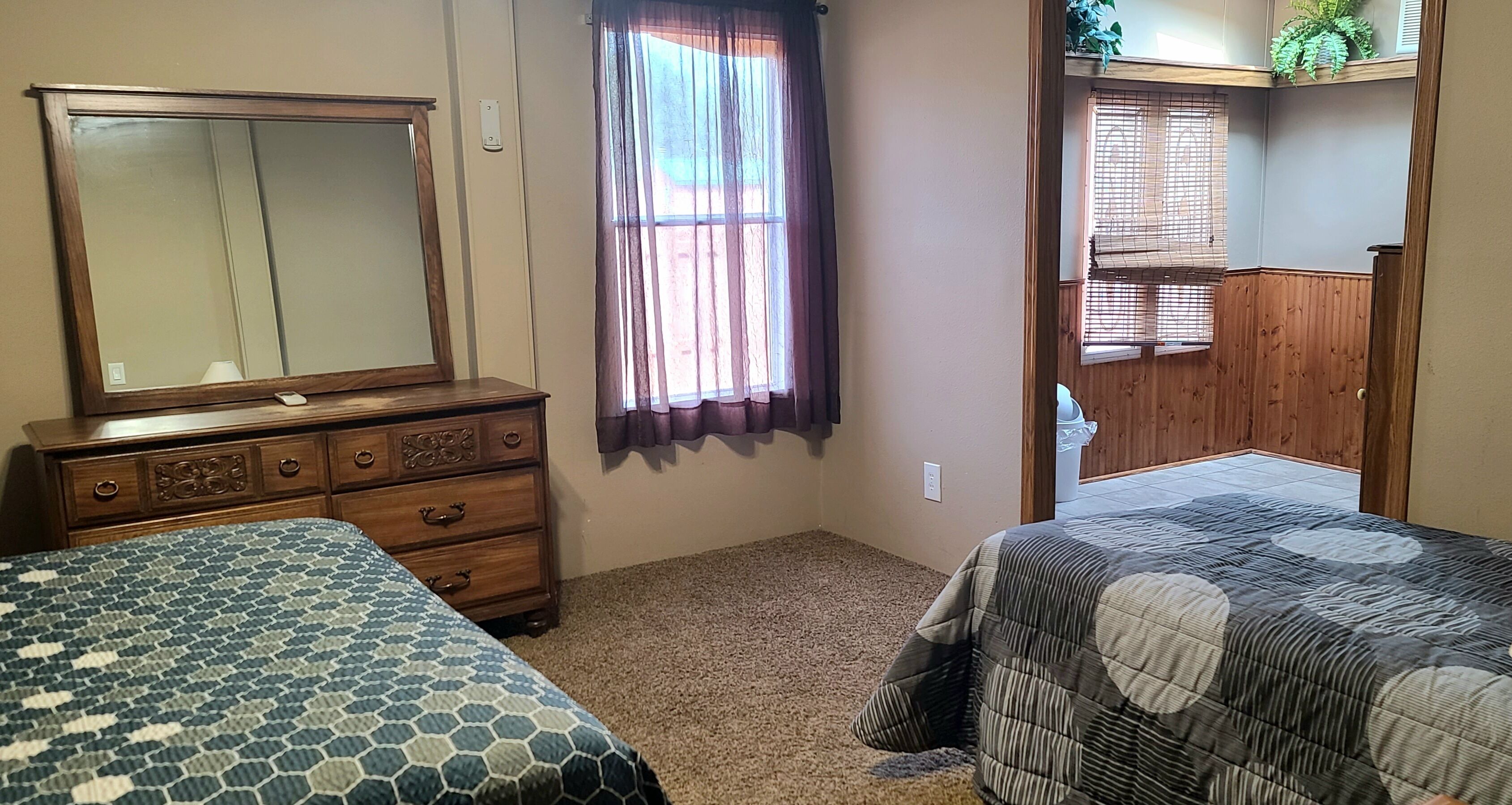 A bedroom with two beds, a dresser, a mirror, and a window with curtains.