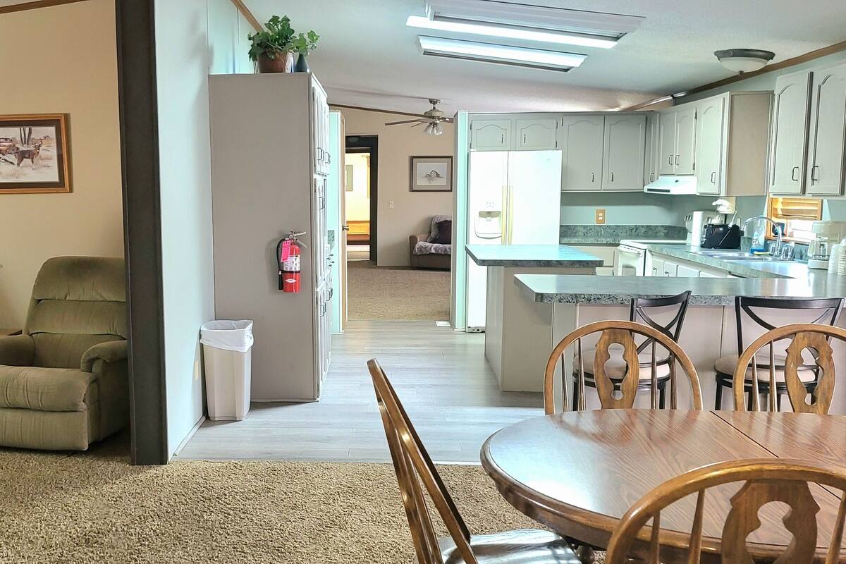 Ein Wohnzimmer mit zwei Sofas, einem Esstisch mit Stühlen, einer Küche inklusive Kühlschrank und Schränken sowie einem Flur, der in ein weiteres Zimmer führt.