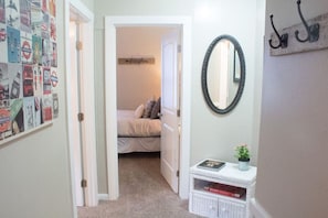 A bedroom with a bed, a small bedside table with a book and a plant, a mirror on the wall, and a door leading to another room. - Heart of Downtown 2-Bedroom Apt, Mountain Views, Full Kitchen, Walk to Eats (Glenwood Springs)