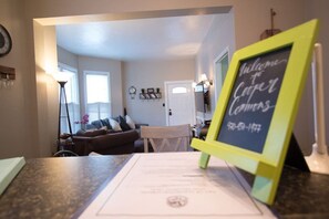 A living room with a couch, a coffee table, and a chalkboard sign that reads 'Welcome to Cooper Commons.' - Heart of Downtown 2-Bedroom Apt, Mountain Views, Full Kitchen, Walk to Eats (Glenwood Springs)