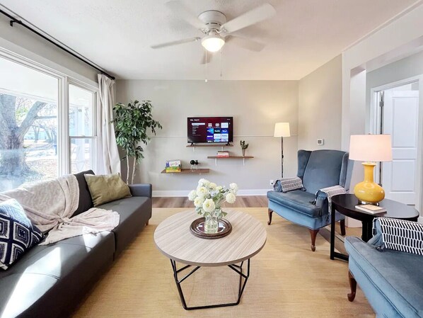 A modern living room with a sofa, armchairs, a coffee table, and a TV mounted on the wall. - Katy Trail Rest Stop (Sedalia)
