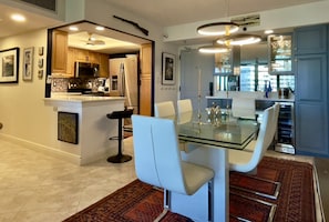Una cocina moderna con electrodomésticos de acero inoxidable, una mesa de comedor de vidrio y sillas blancas.