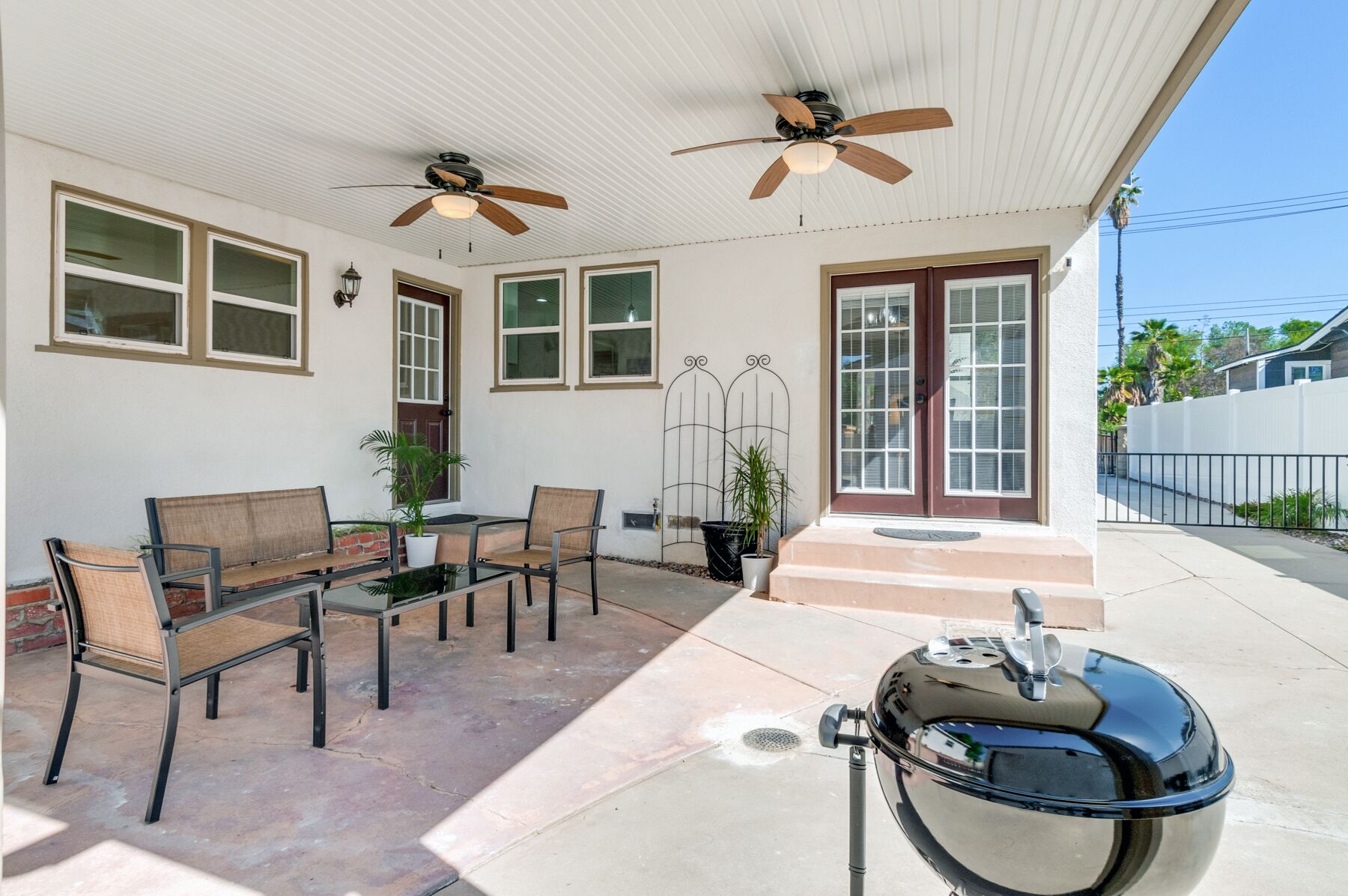 A covered patio area with a table and chairs, ceiling fans, and a barbecue grill.