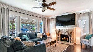 Ein modernes Wohnzimmer mit Kamin, Deckenventilator und großem Fernseher.