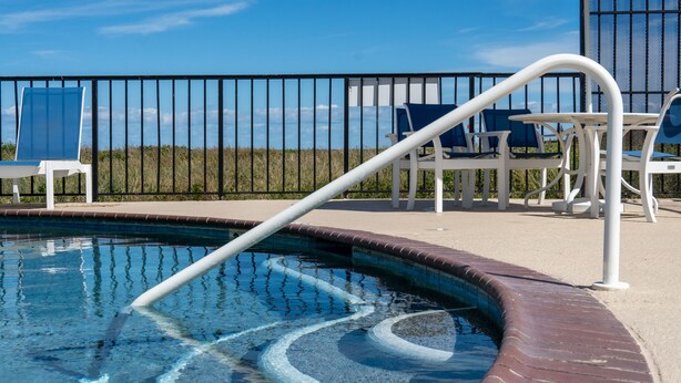Zona de piscina con vista despejada al cielo, una cerca metálica y sillones de descanso.