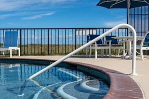 A pool area with a clear view of the sky, a metal fence, and lounge chairs.
