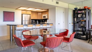 Una cocina moderna con electrodomésticos de acero inoxidable, una mesa de comedor de vidrio y sillas rojas, además de una estantería negra.