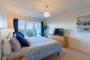 Ein Schlafzimmer mit Bett, Fernseher, Kommode und einem Fenster mit Vorhängen.
