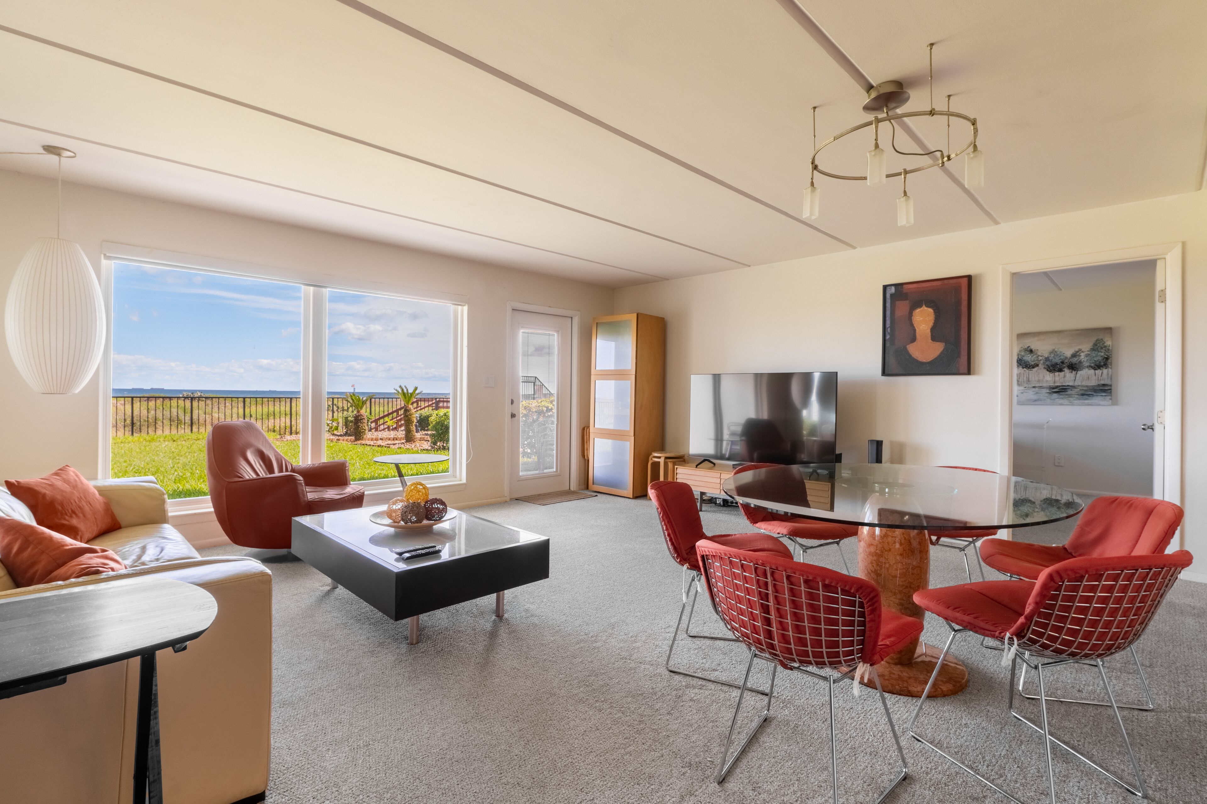 A modern living room with a glass dining table, red chairs, a sofa, and a TV.