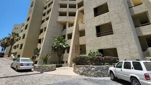 Een meerlaags hotel met een modern architectonisch ontwerp, met balkons en een parkeerplaats met auto's.