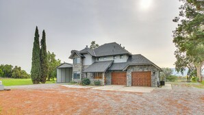 Een twee verdiepingen tellend stenen huis met een stenen garage, een grindpad en hoge bomen op de achtergrond.