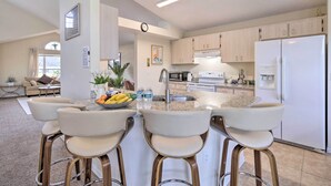 A modern kitchen with a central island, bar stools, and a refrigerator. - 5 Mi to Disney! Family Getaway w/ Poolside Oasis (Kissimmee)