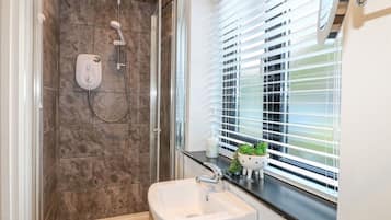A modern bathroom with a shower, a sink, and a window with blinds.
