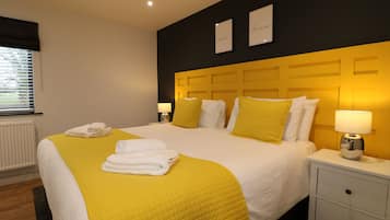 Une chambre d’hôtel comprenant un lit, deux tables de chevet, une fenêtre avec des stores et un mur orné de deux tableaux encadrés.