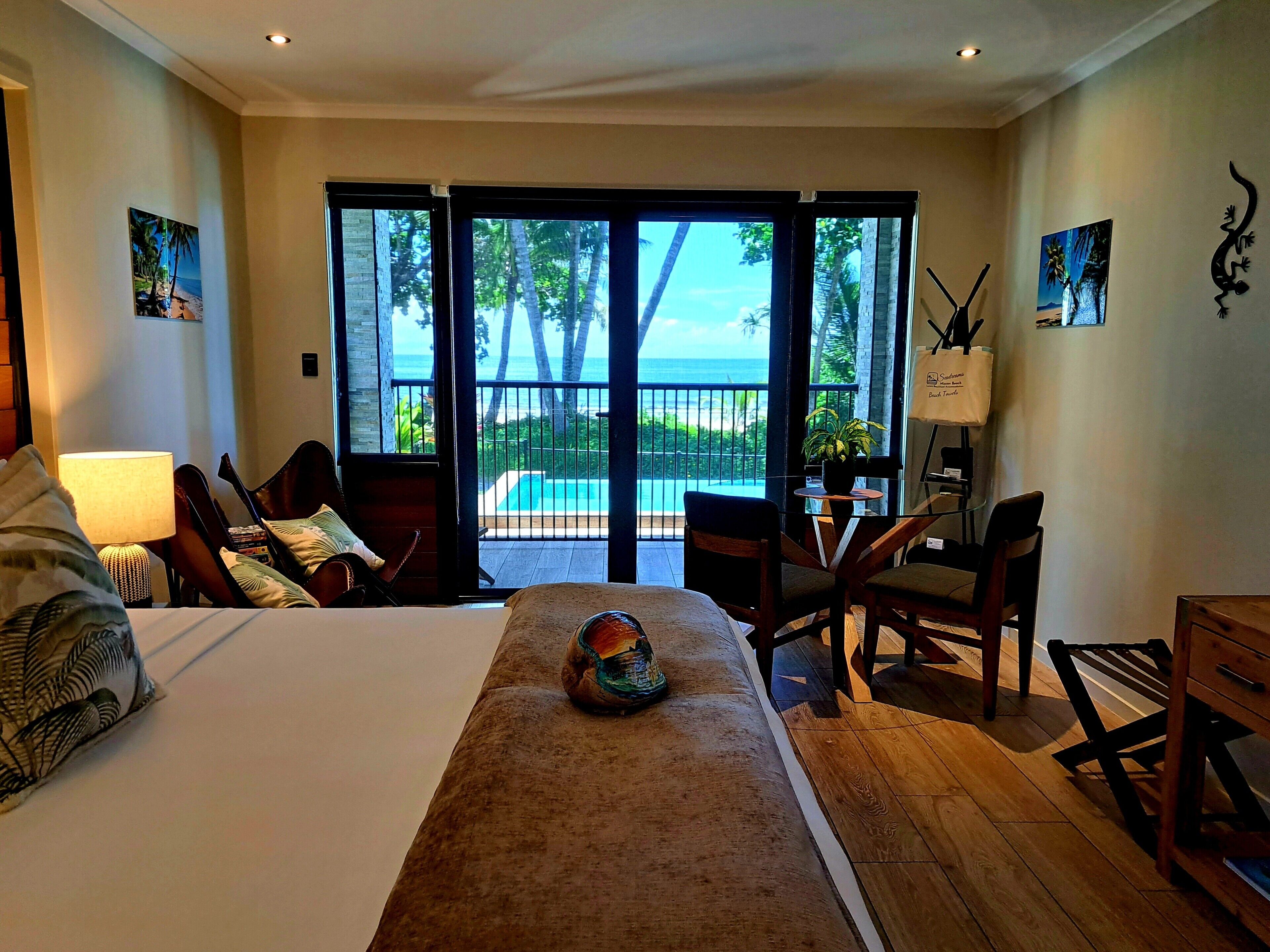 A hotel room with a bed, a desk, a chair, and a view of the ocean through large sliding doors.