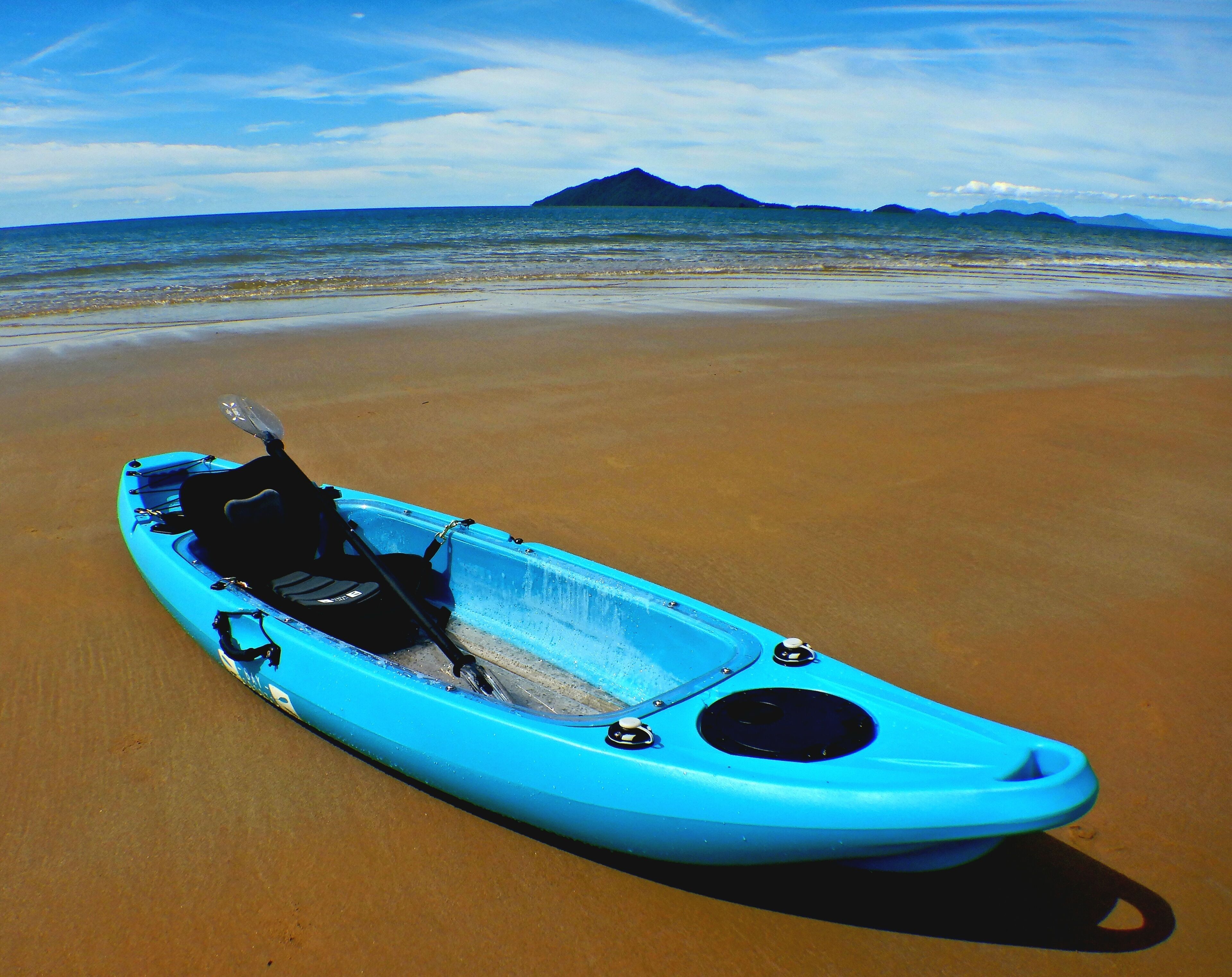 Un kayak bleu sur une plage de sable, avec une montagne en arrière-plan.