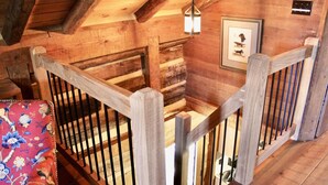 A wooden staircase with a railing, a hanging light fixture, and a framed picture on the wall.