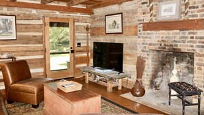 A rustic cabin interior with a wooden bench, leather chair, fireplace, and framed pictures on the walls.