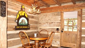 A wooden interior with a round wooden table, four wooden chairs, a chandelier, and a door with a window.