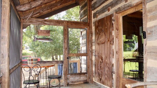 A wooden cabin with a porch, a table with chairs, and a hanging light fixture.