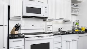 Een moderne keuken met witte kastjes, een ingebouwde magnetron, een fornuis en een koffiezetapparaat.