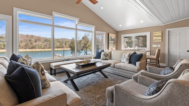 Un vaste salon doté de grandes fenêtres, d’un ventilateur de plafond et offrant une vue sur un lac.